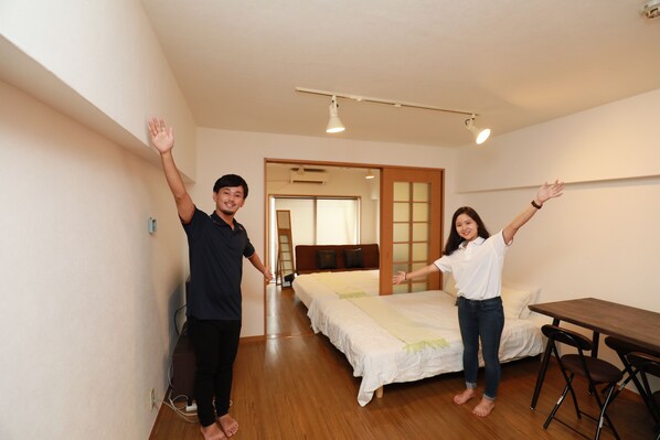 A room with two beds, a wooden table, and a small seating area. - IBASHO Shibuya Higashi 604 (Tokyo)