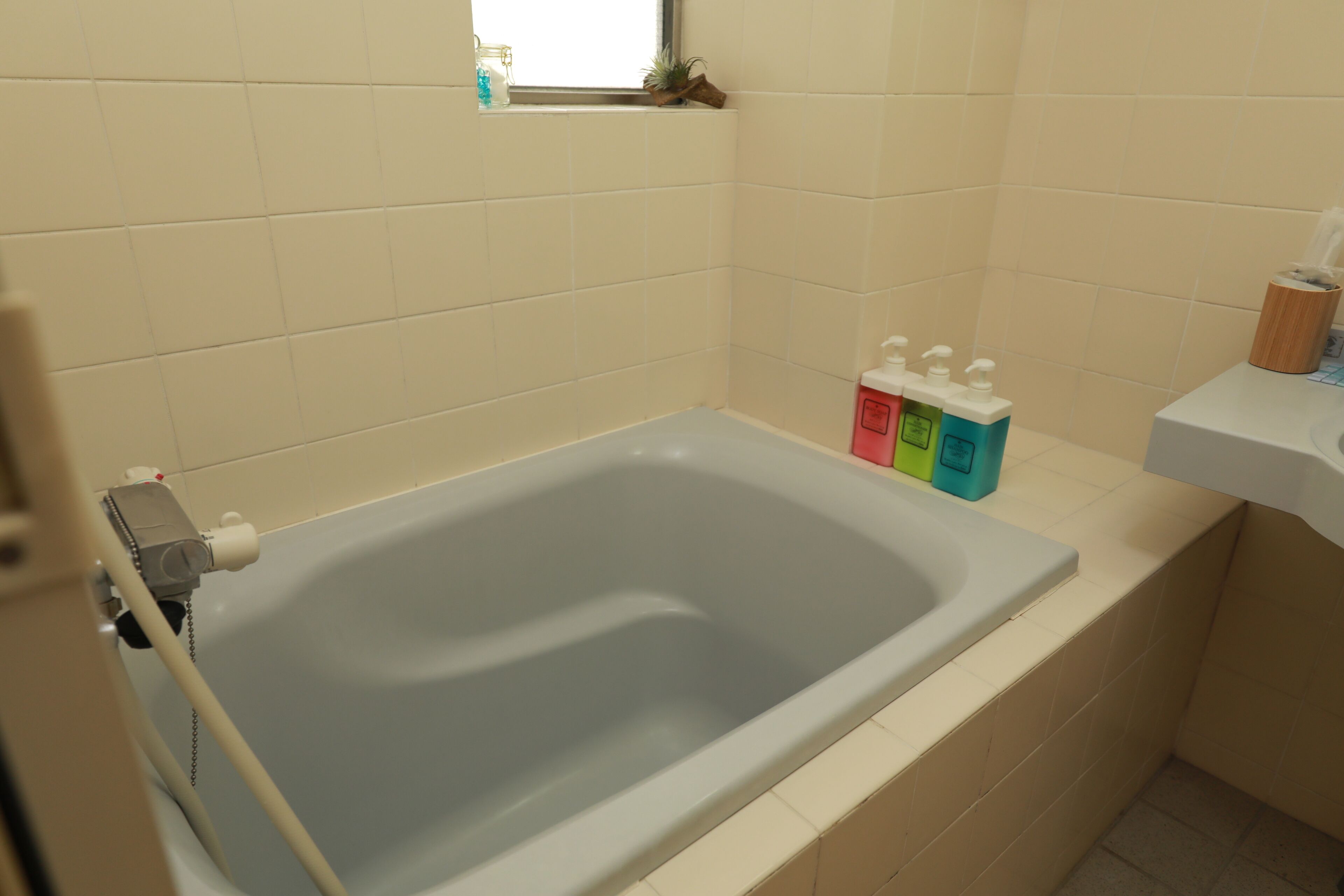 A bathroom with a bathtub, a window, and toiletries on the counter.
