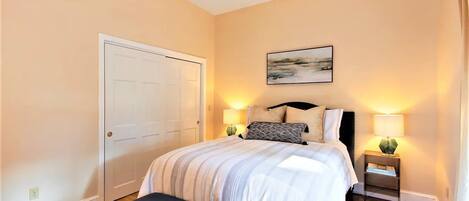 A bedroom with a bed, bedside tables, a bench, and a door.