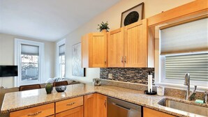 Una cocina moderna con gabinetes de madera, encimeras de granito, lavavajillas y una ventana con persianas.