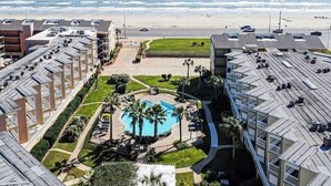 Um hotel com piscina no terraço, vista para a praia e estacionamento.
