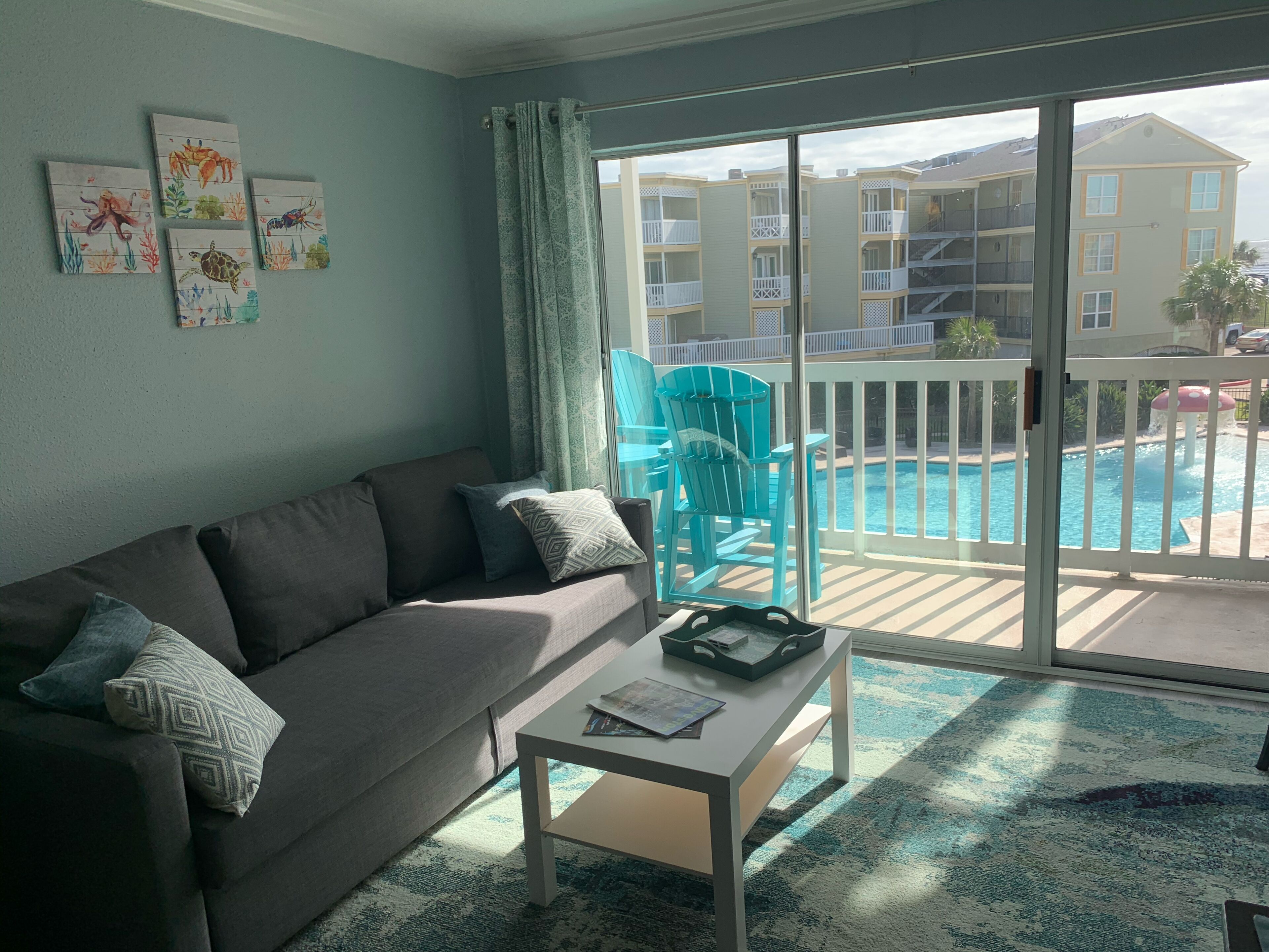 A living room with a gray sofa, a coffee table, and a view of a pool and buildings.