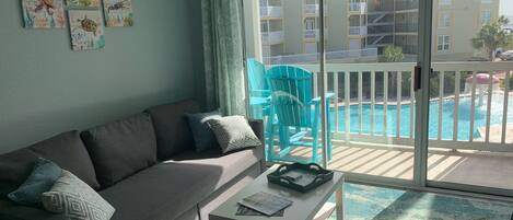 A living room with a gray sofa, a coffee table, and a view of a pool and buildings.