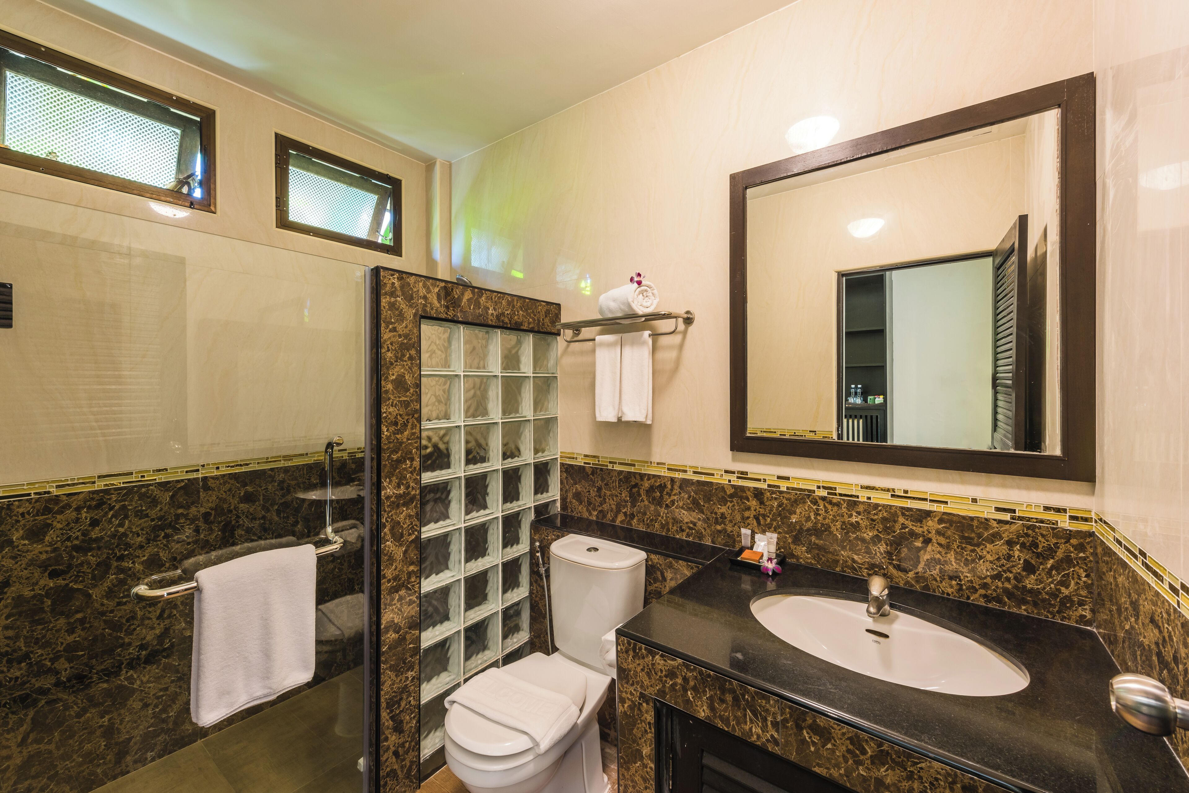 A bathroom with a glass shower enclosure, a toilet, a sink with a mirror above it, and a towel rack with towels.
