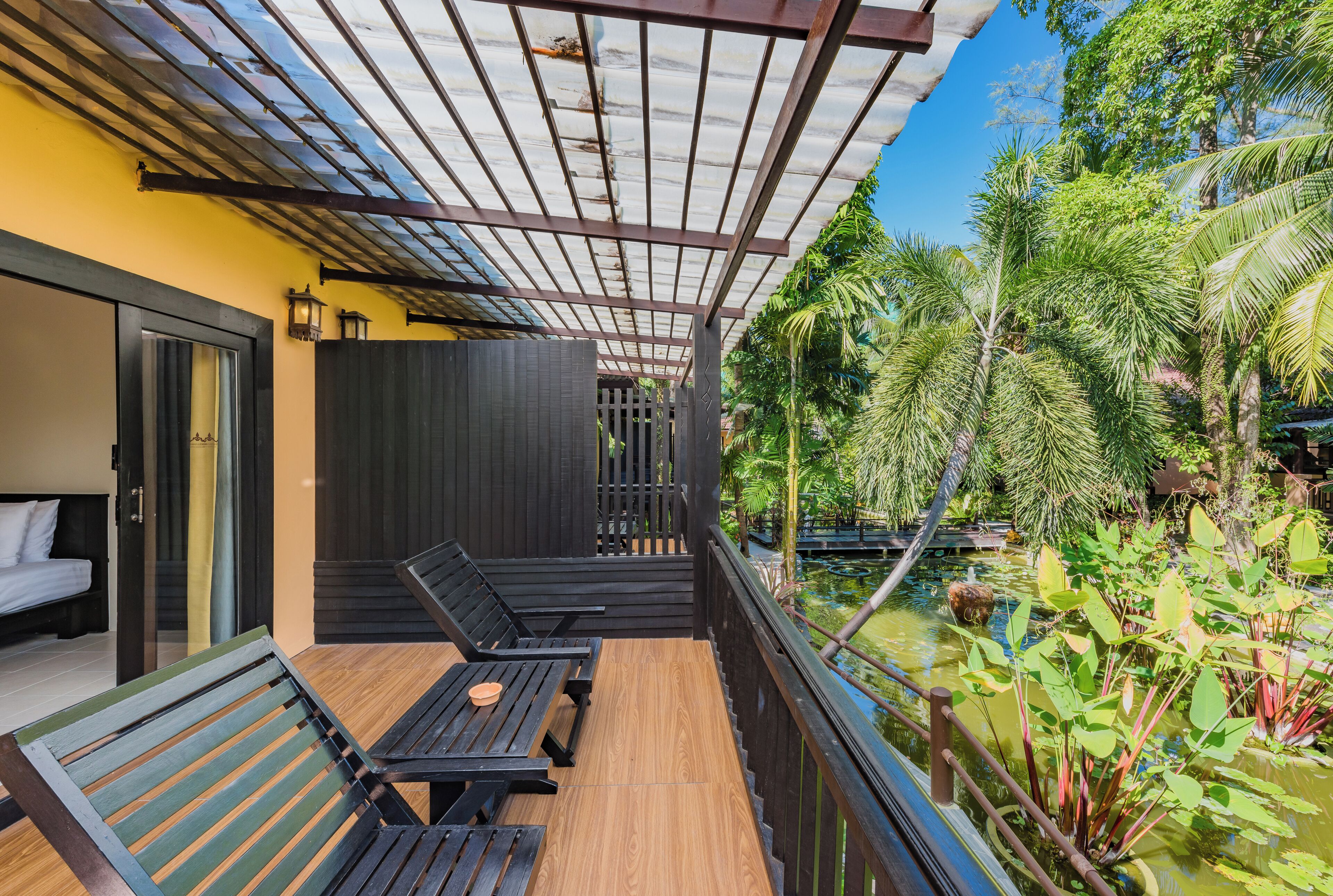 A balcony with wooden flooring, two black lounge chairs, a small table, and a glass door leading to a bedroom.