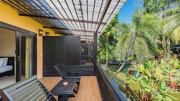 A balcony with wooden flooring, two black lounge chairs, a small table, and a glass door leading to a bedroom.