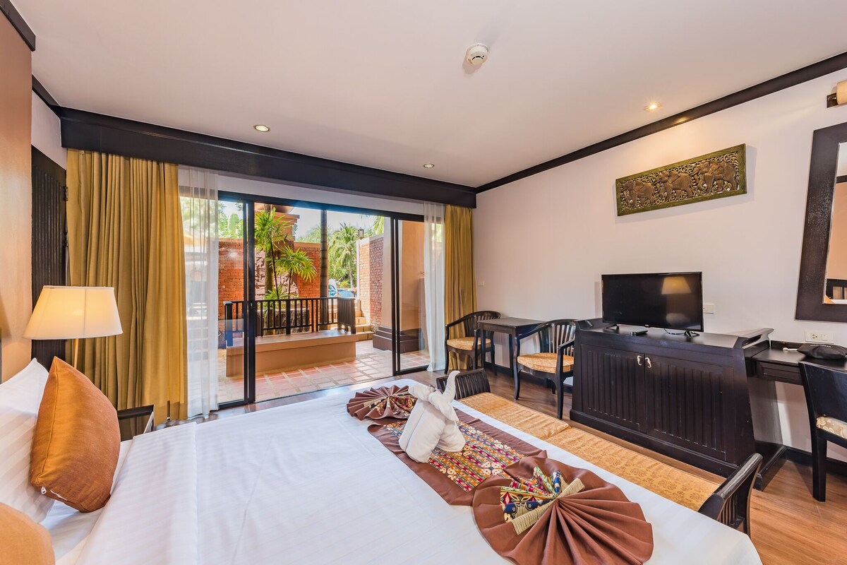 Habitación de hotel con cama, escritorio, televisor y balcón con vistas al exterior.