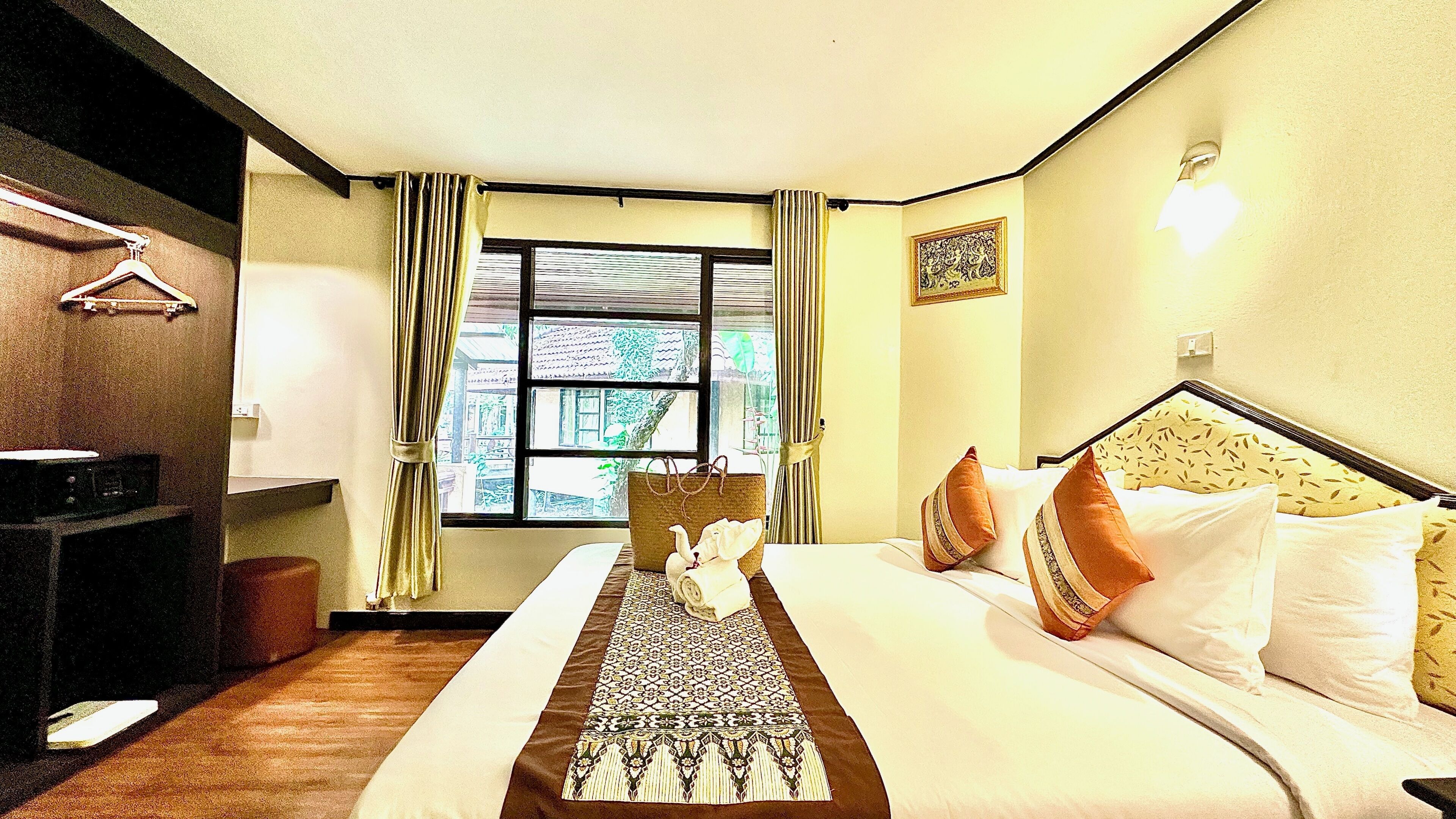A hotel room with a bed, a bedside table, a window with curtains, a wall-mounted light, and a framed picture.