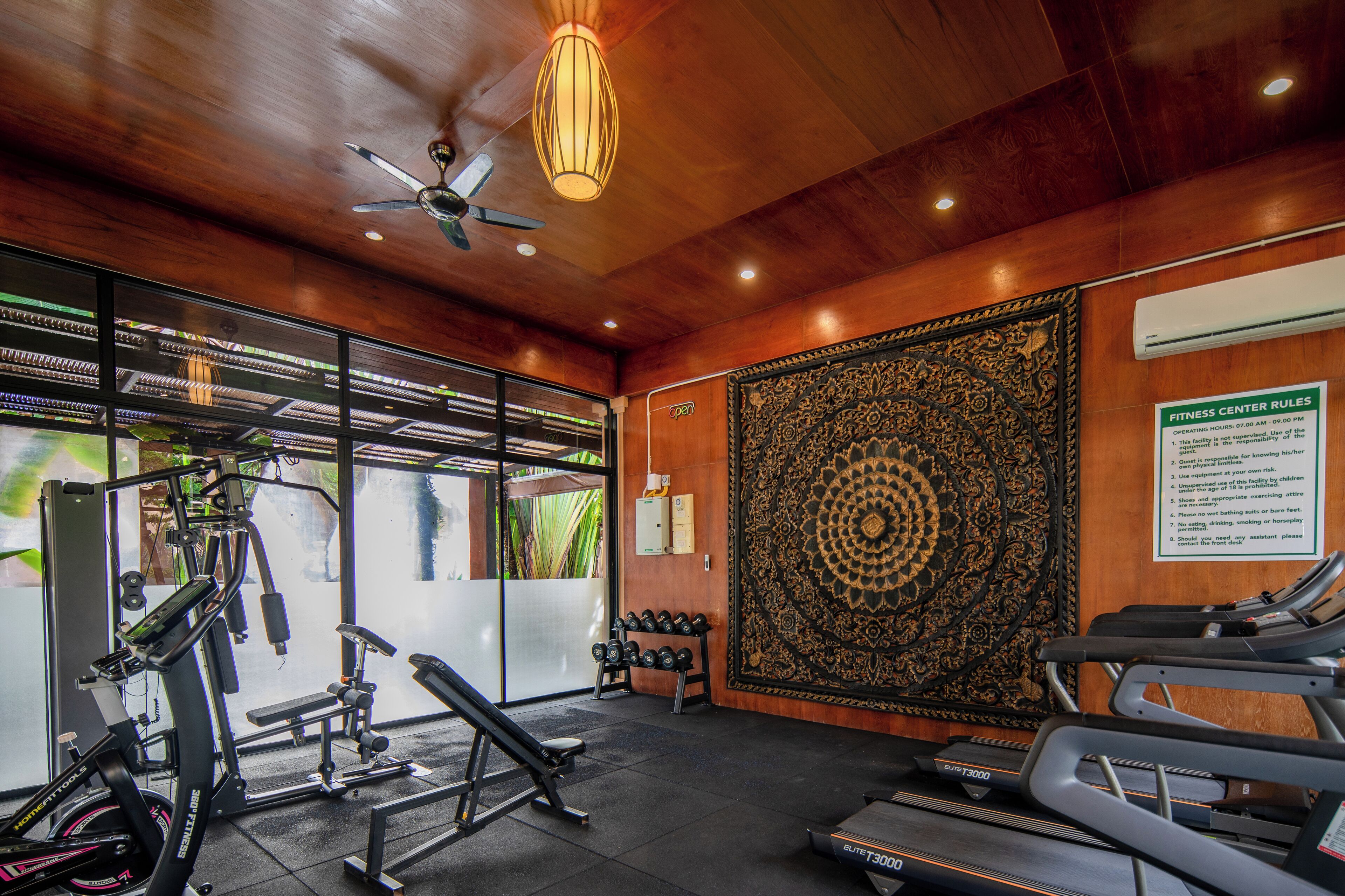 A gym with exercise equipment, a large decorative wall, and a ceiling fan.