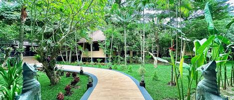 A wooden pathway leading to a building surrounded by lush greenery and tropical plants.