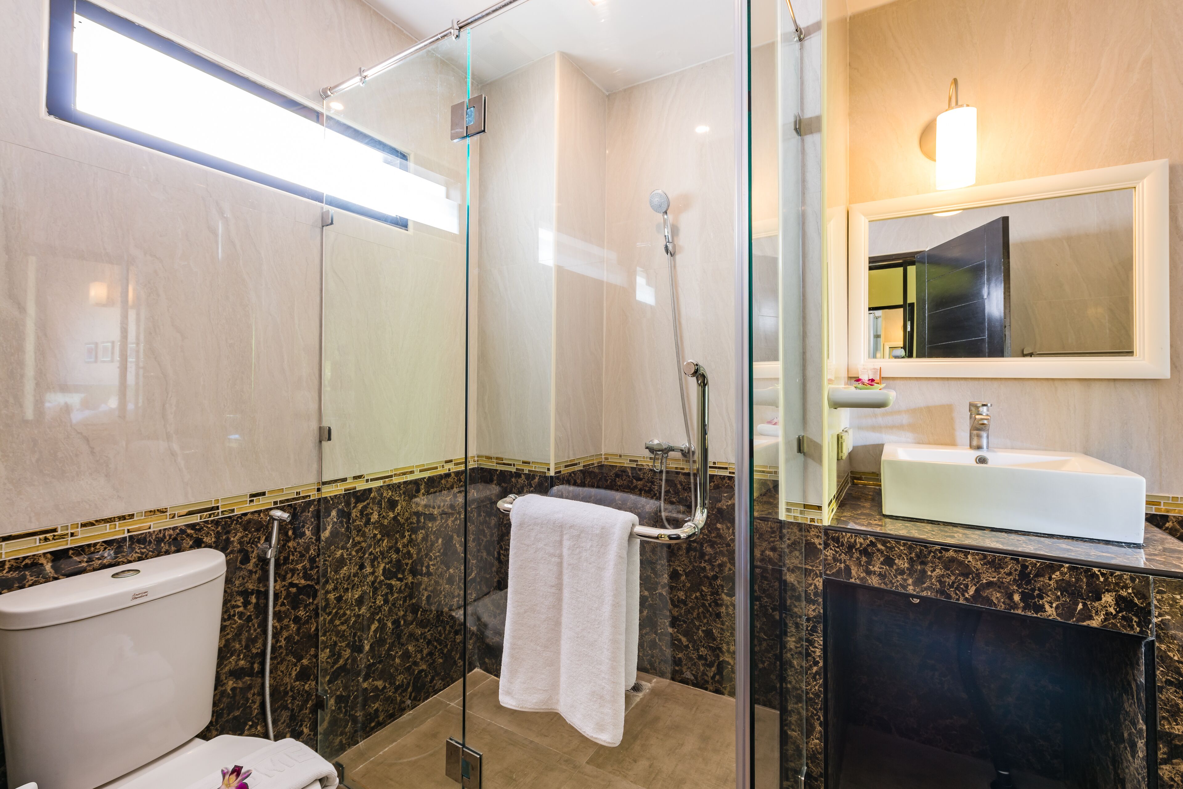 A modern bathroom with a glass-enclosed shower, a white toilet, and a marble-tiled vanity with a sink.