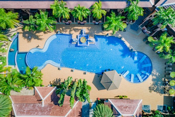 An aerial view of a resort with a large central pool, surrounded by palm trees and lounge areas.
