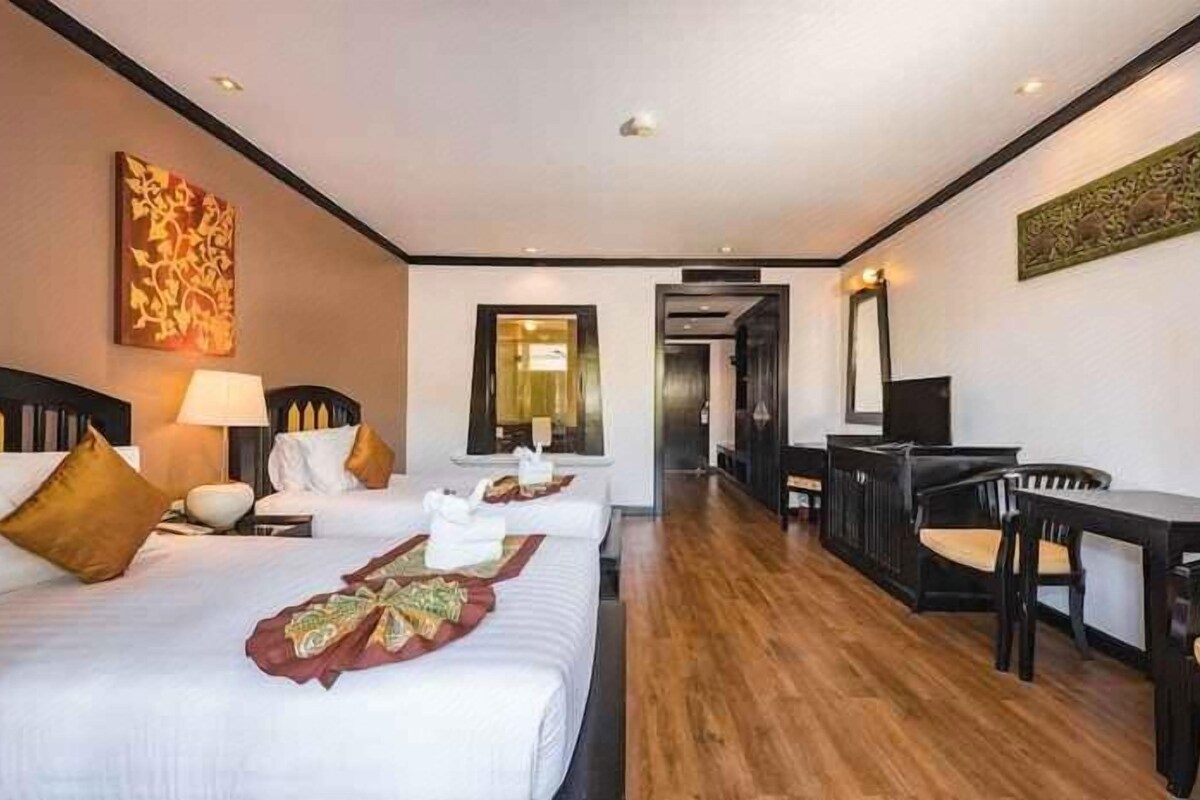 Ein Hotelzimmer mit drei Betten, einem Schreibtisch und einem Sessel.