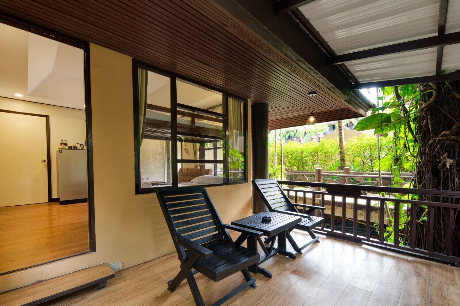 A balcony with wooden flooring, two black lounge chairs, and a view of greenery and a building in the background.