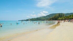 A beach with clear turquoise water, people swimming and sunbathing, and a line of palm trees on the shore. - Princess Kamala Beachfront Hotel (Kamala)