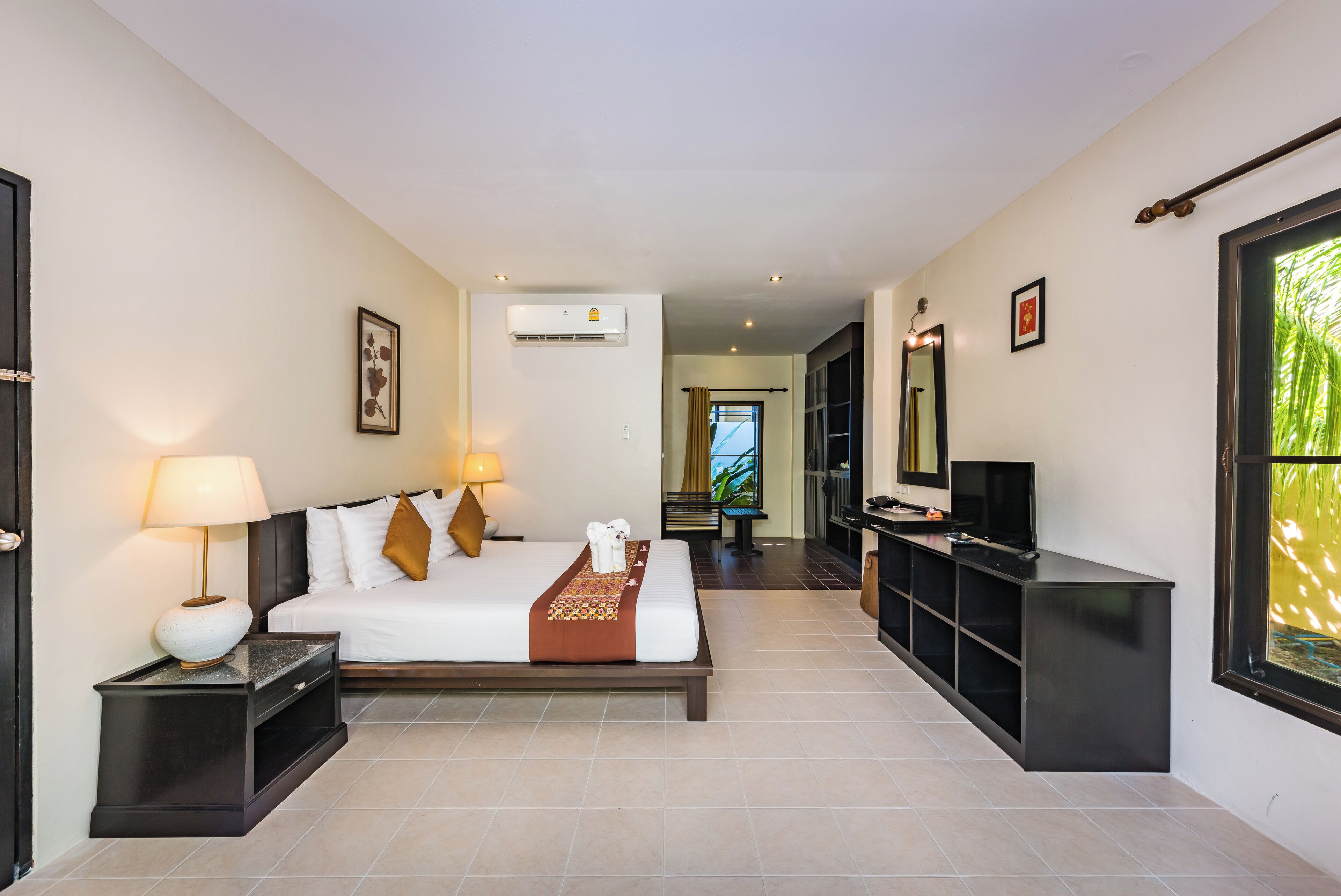 A hotel room with a bed, bedside table, lamp, air conditioning unit, and a television.