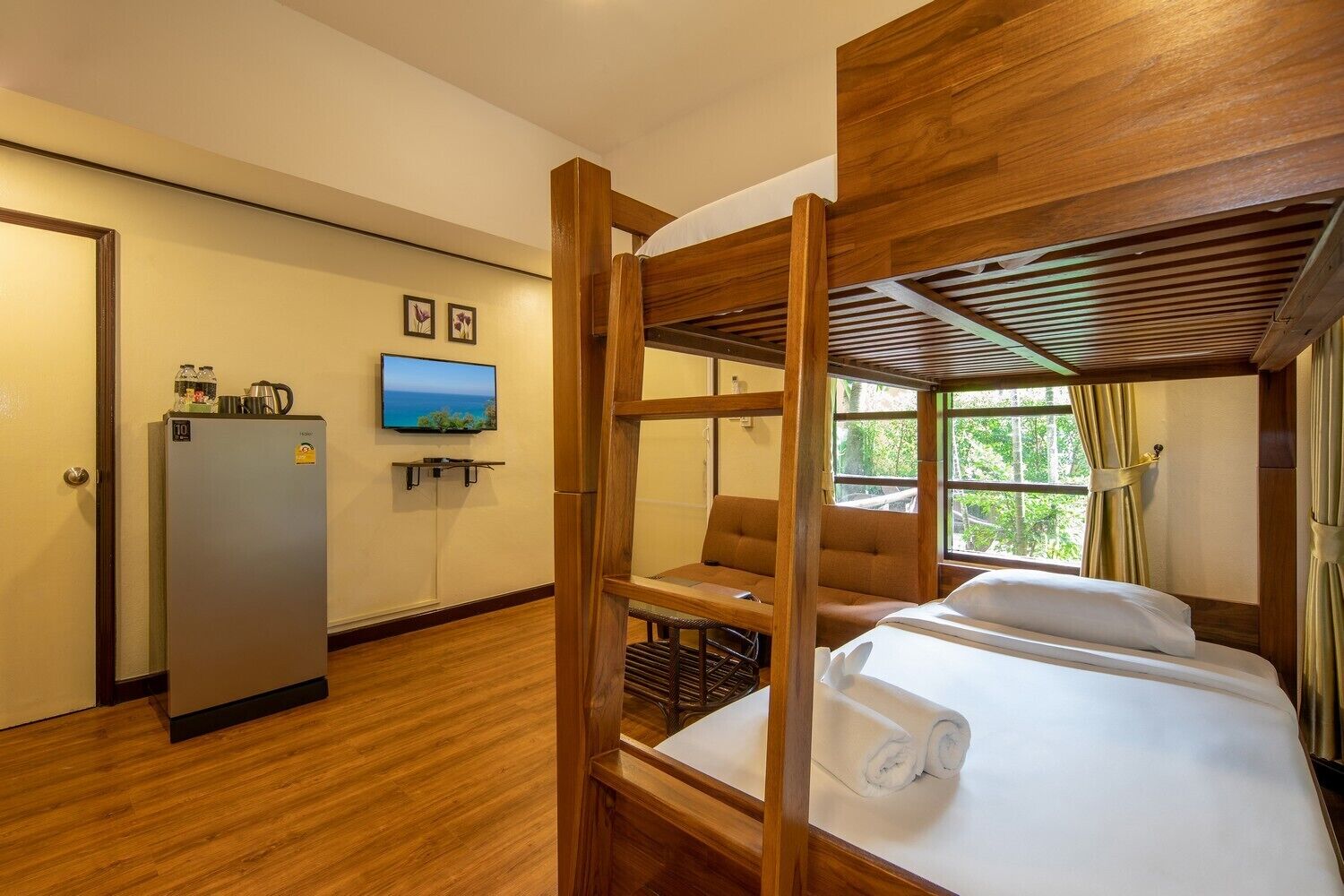 A compact hotel room with a bunk bed, a sofa, a television, and a refrigerator.