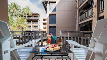 A balcony with a table set for breakfast, including a bottle of wine, fruit, and a drink.