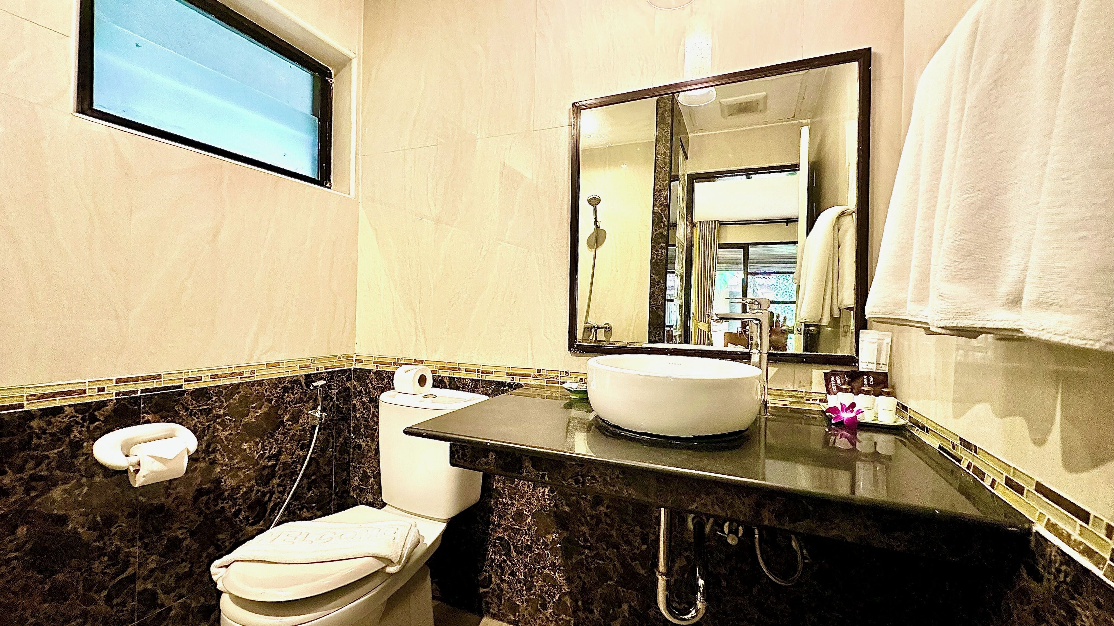 A bathroom with a marble sink, a toilet, a mirror, and a window.