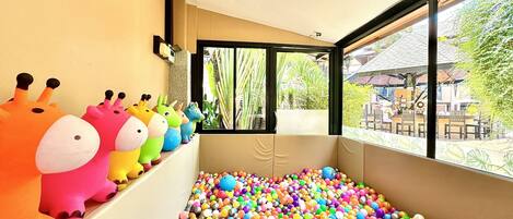 A room with a ball pit filled with colorful balls, a window with a view of the outside, and a wall with plush toys.
