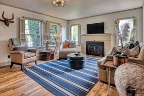 A living room with a fireplace, a television, and a large window with shutters. - 5 Bedroom, 3 Bath House! With Brand New Hot Tub! (Eugene)