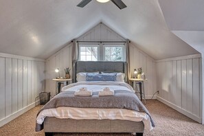 Une chambre avec un plafond en pente, un grand lit, deux tables de chevet avec des lampes et une fenêtre.