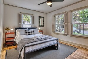 Ein Schlafzimmer mit einem Bett, Nachttischen, einem Deckenventilator und Fenstern mit Rollläden.