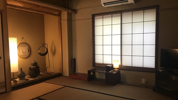 A traditional Japanese room with tatami flooring, a shoji screen, a television, and a small table with a lamp. - Uego (Niijima)