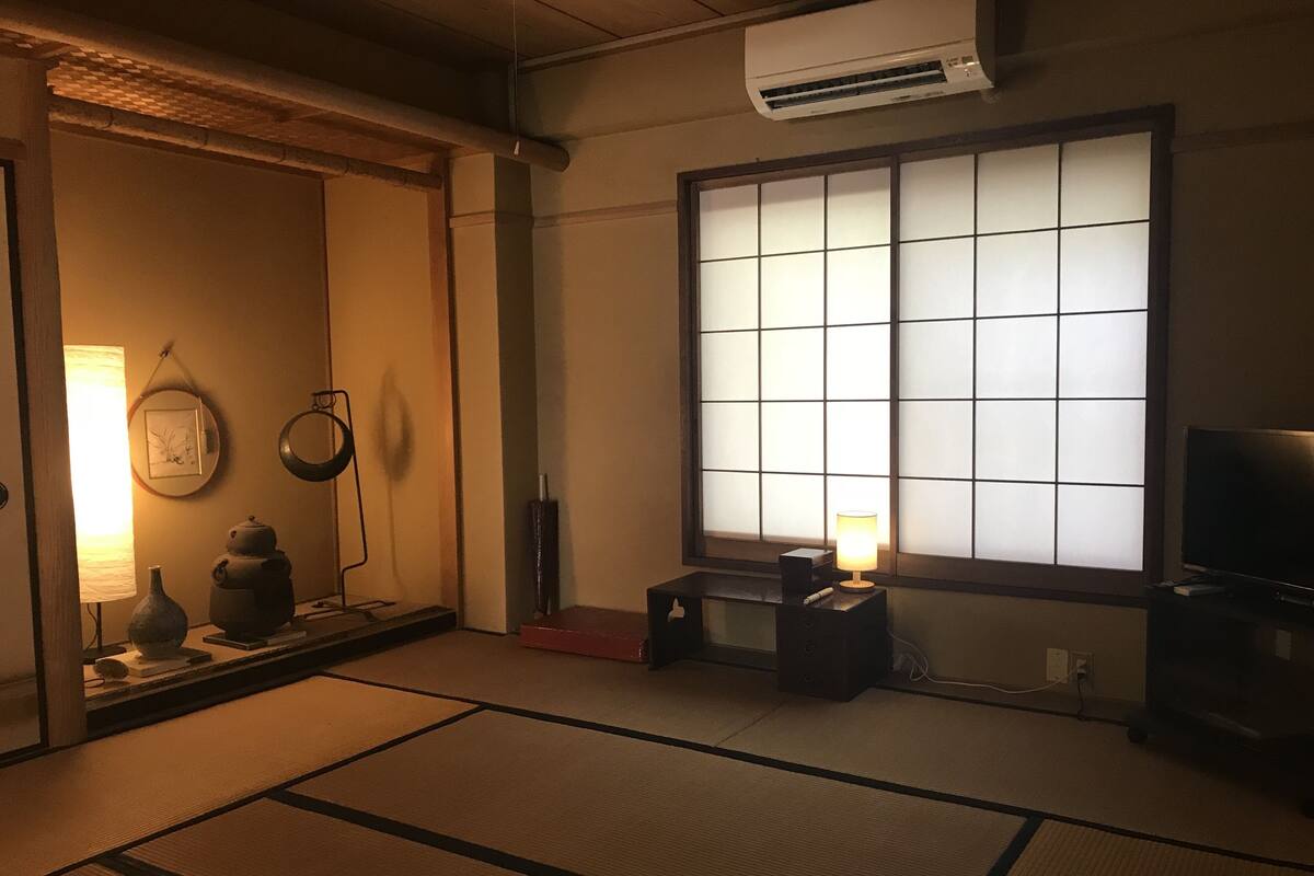 Ein traditioneller japanischer Raum mit Tatami-Boden, Shoji-Schirm, Fernseher und einem kleinen Tisch mit Lampe.