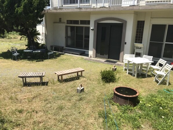 A backyard with a wooden bench, a small garden, and a patio area with white chairs and a table.
