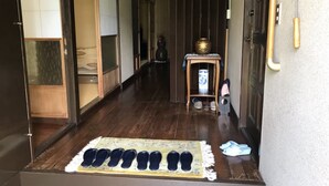 A traditional Japanese entrance with a wooden floor, a tatami mat, and a small table with a vase. - Uego (Niijima)