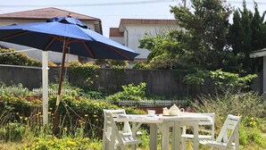 A white outdoor table with chairs, a blue umbrella, and a white fence in a garden setting. - Uego (Niijima)