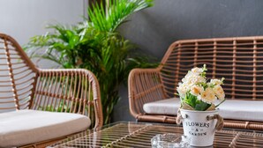Wicker furniture with cushions, a glass table, and a bucket labeled "FLOWERS & GARDEN" with flowers. - Aspira Gems Center Silom (Bangkok)