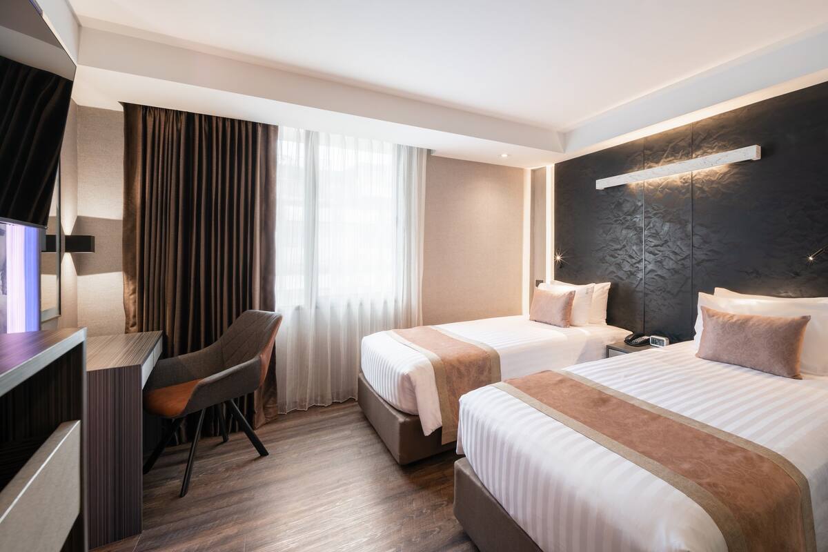 A hotel room with two beds, a desk, and a chair.