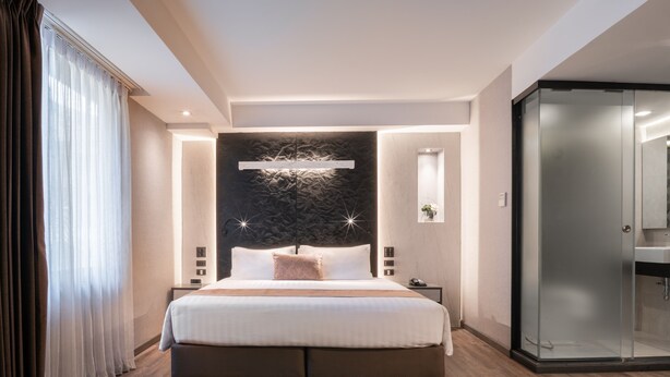 A modern hotel bedroom with a large bed, bedside tables, a glass shower enclosure, and a stone accent wall. - Aspira Gems Center Silom (Bangkok)