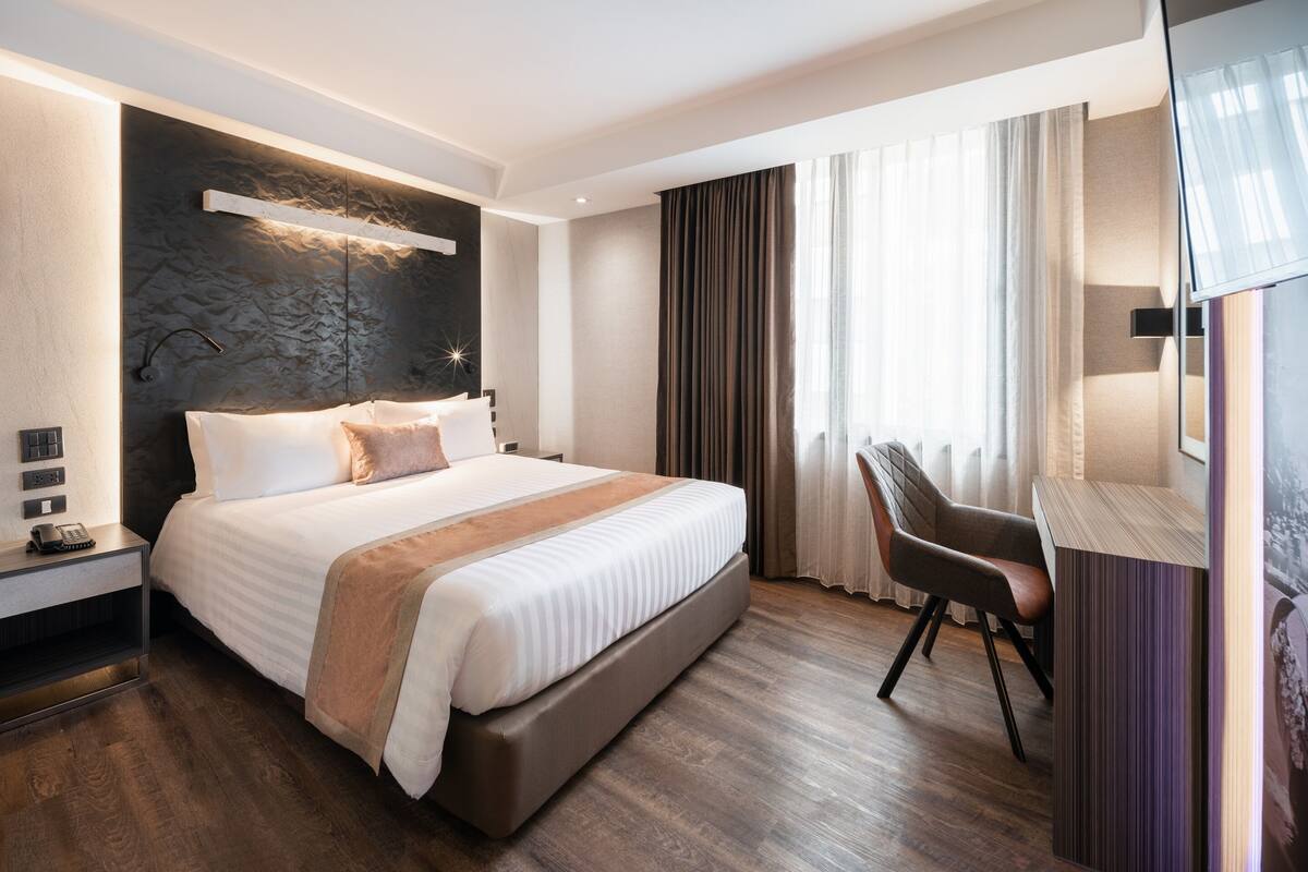 A modern hotel room with a large bed, a desk, and a chair.