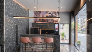 A modern bar area with marble walls, a digital screen, and three cushioned bar stools. - Aspira Gems Center Silom (Bangkok)