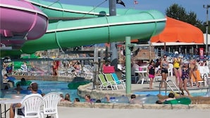 Parque acuático con múltiples toboganes y piscinas, rodeado de sillas de playa y sombrillas.