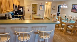 Een keuken met houten kasten, een roestvrijstalen koelkast en een eethoek met houten stoelen en een tafel.