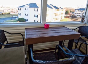 Een balkon met een tafel en stoelen, uitkijkend op een woongebied met appartementen.