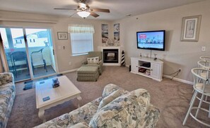 A living room with a sofa, ottoman, coffee table, fireplace, TV, and a ceiling fan.
