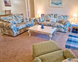 Een woonkamer met sofabekleding met bloemenprint, een witte salontafel en een groene fauteuil.