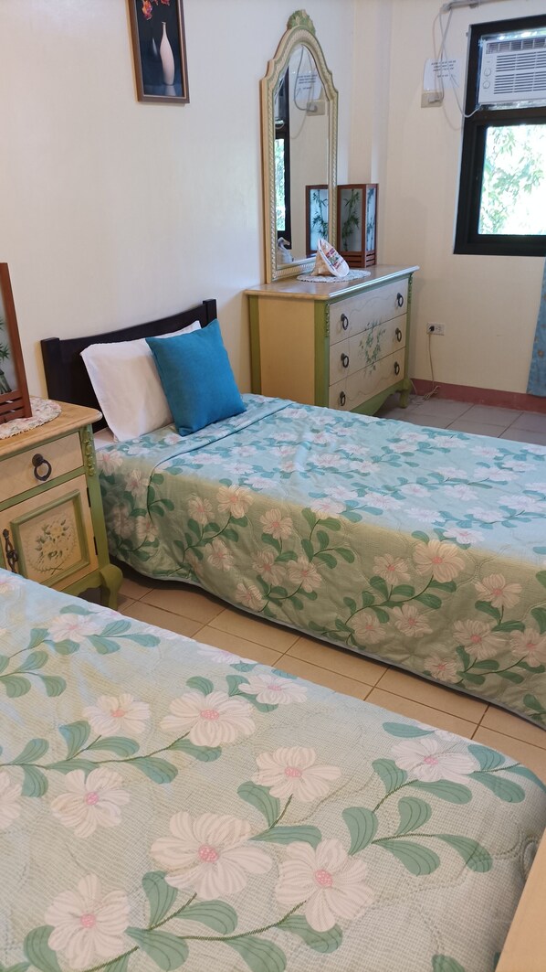 A bedroom with two beds, a dresser, a mirror, and a window.