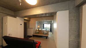 Ein modernes Hotelzimmer mit einer Couch, einem kleinen Tisch und einem Bett. Ein Flur führt zu einem Balkon mit Blick.
