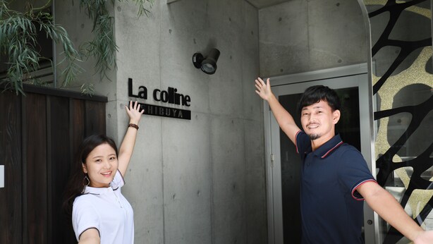 Ein Mann und eine Frau stehen vor einem Gebäude, an dem ein Schild mit der Aufschrift "La coline" zu sehen ist.