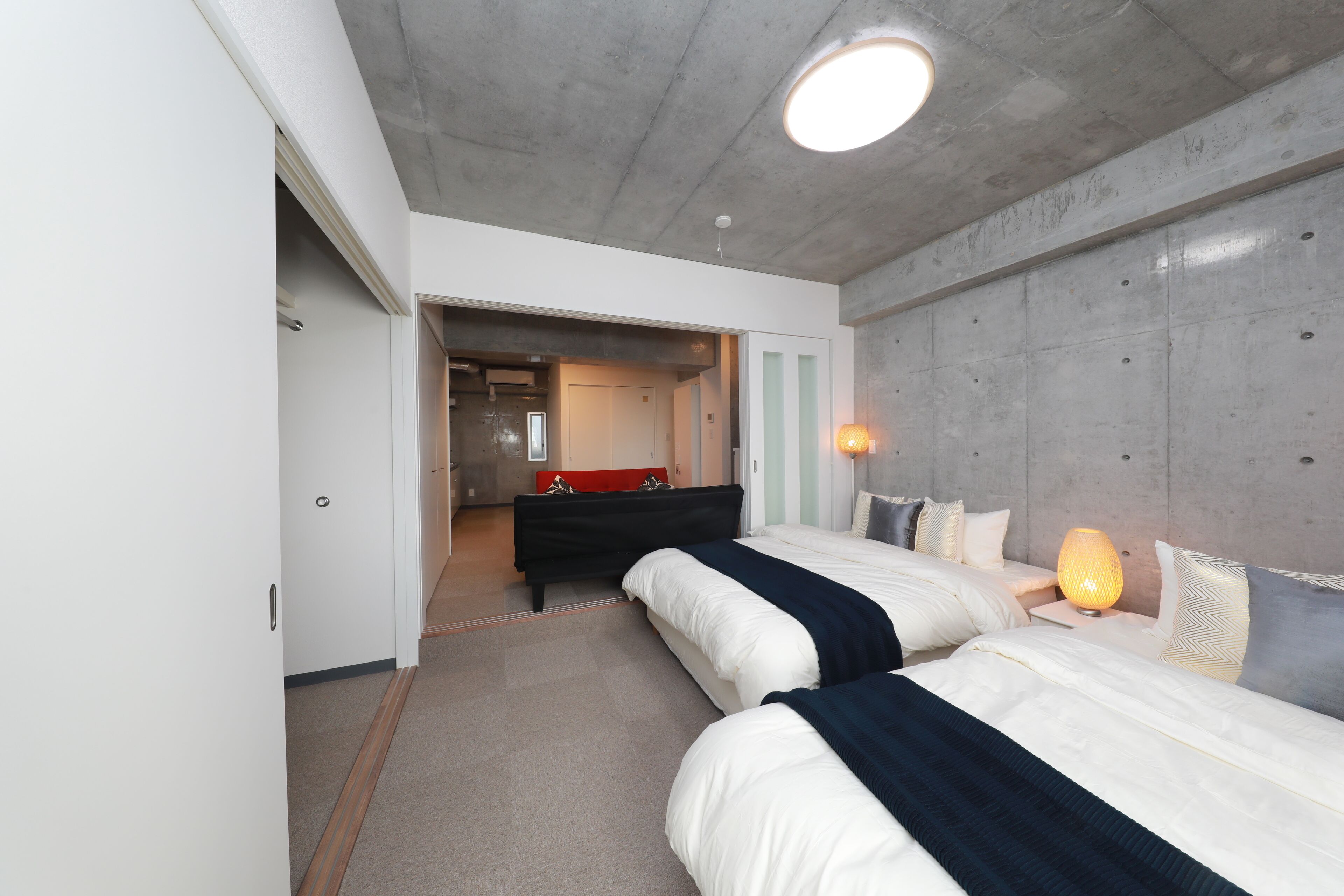 Une chambre d’hôtel moderne avec deux lits, un banc rouge, une lampe et une vue sur le couloir.