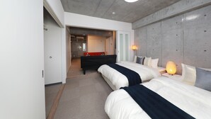 Ein modernes Hotelzimmer mit zwei Betten, einer roten Bank, einer Lampe und Blick auf den Flur.