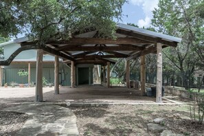 Shaded outdoor space with a covered structure, surrounded by trees and a gravel ground.