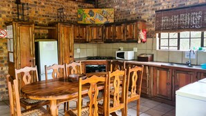 Une cuisine rustique avec des meubles de rangement en bois, une table à manger, des chaises, un réfrigérateur, un four à micro-ondes et une fenêtre.