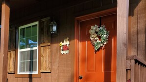 A wooden house with a red door, a window, a small table, a potted plant, and a welcome mat. - The BirdDog Farm Cabin #1        (Dixon Springs)
